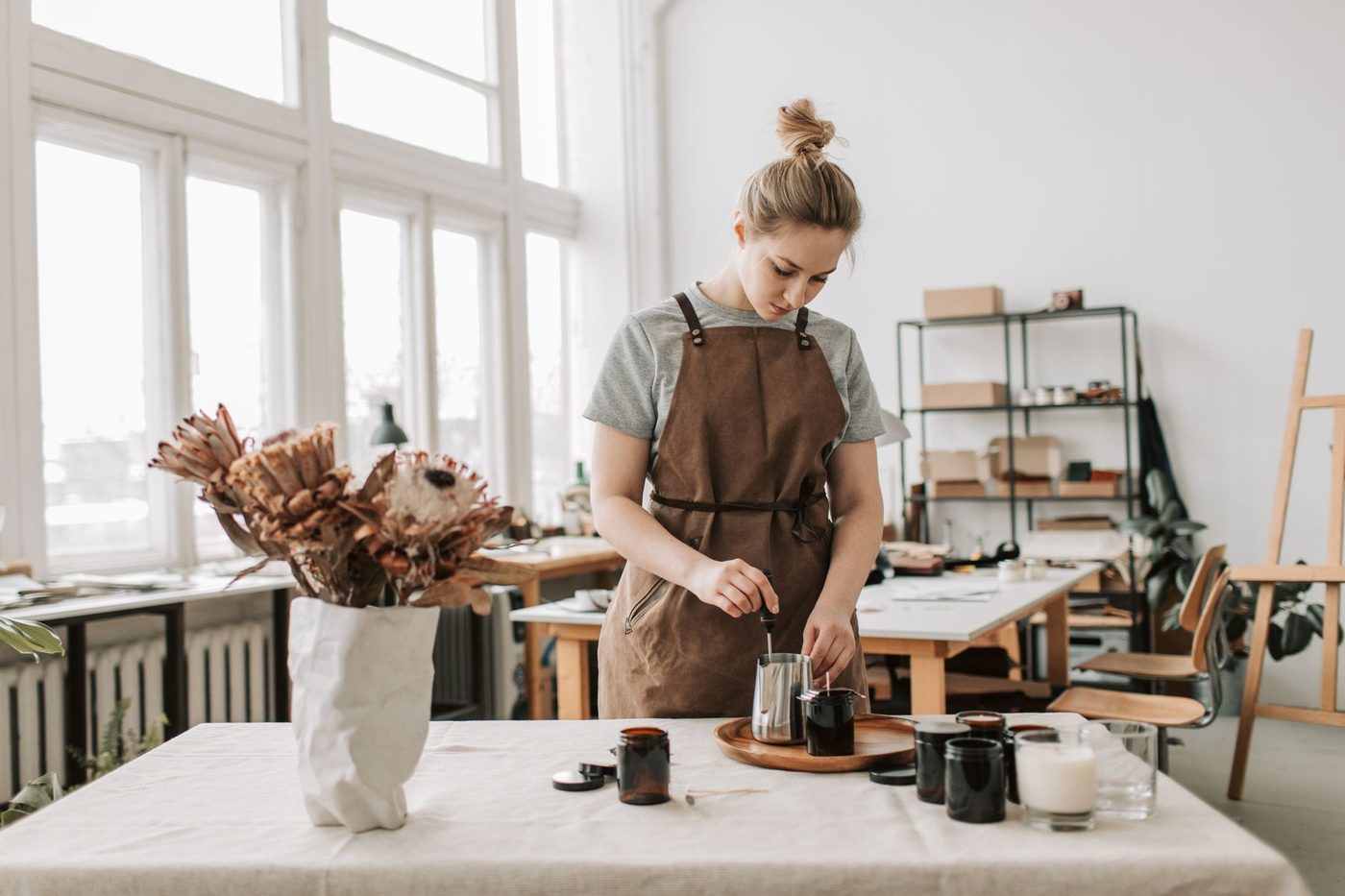 A candle maker filling jars at the table in her workshop