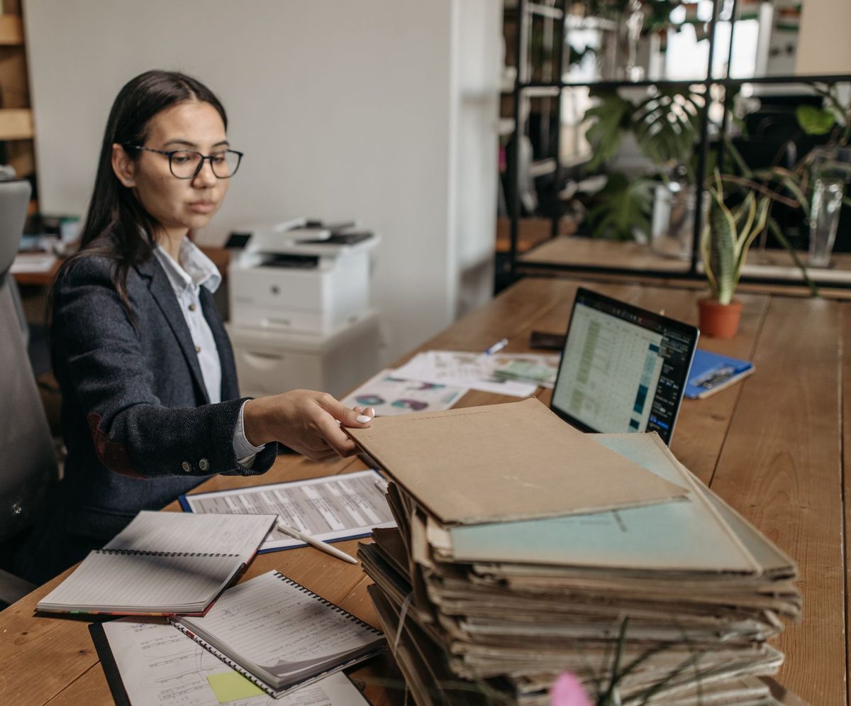 An owner working through a tall stack of company files at her desk