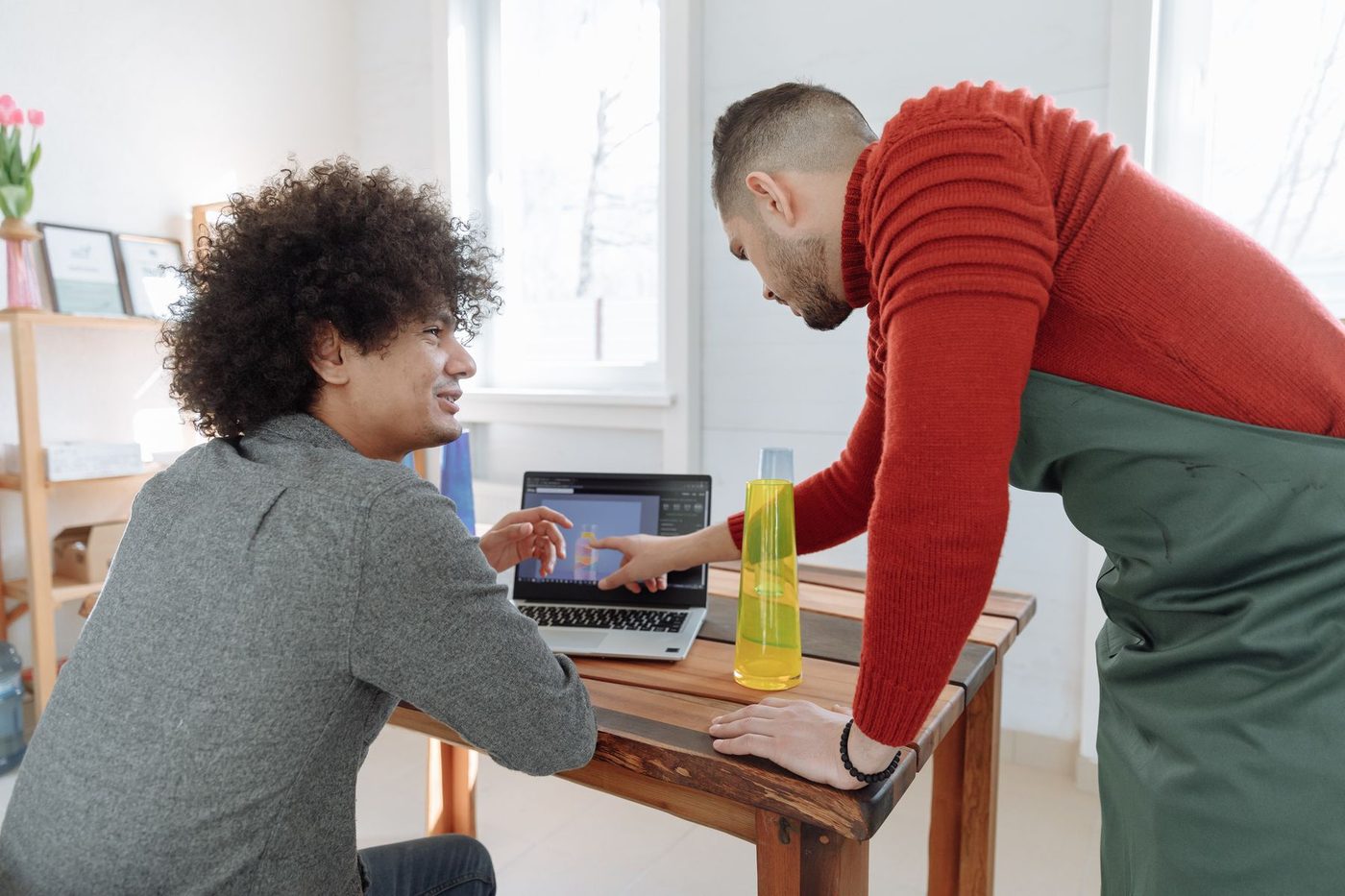 A freelance designer going through work on a laptop with a small business owner in his studio