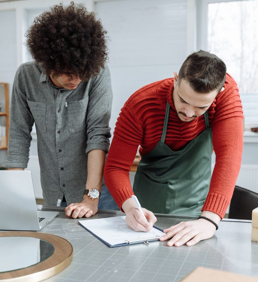 A business owner in an apron signing paperwork while a freelancer looks on