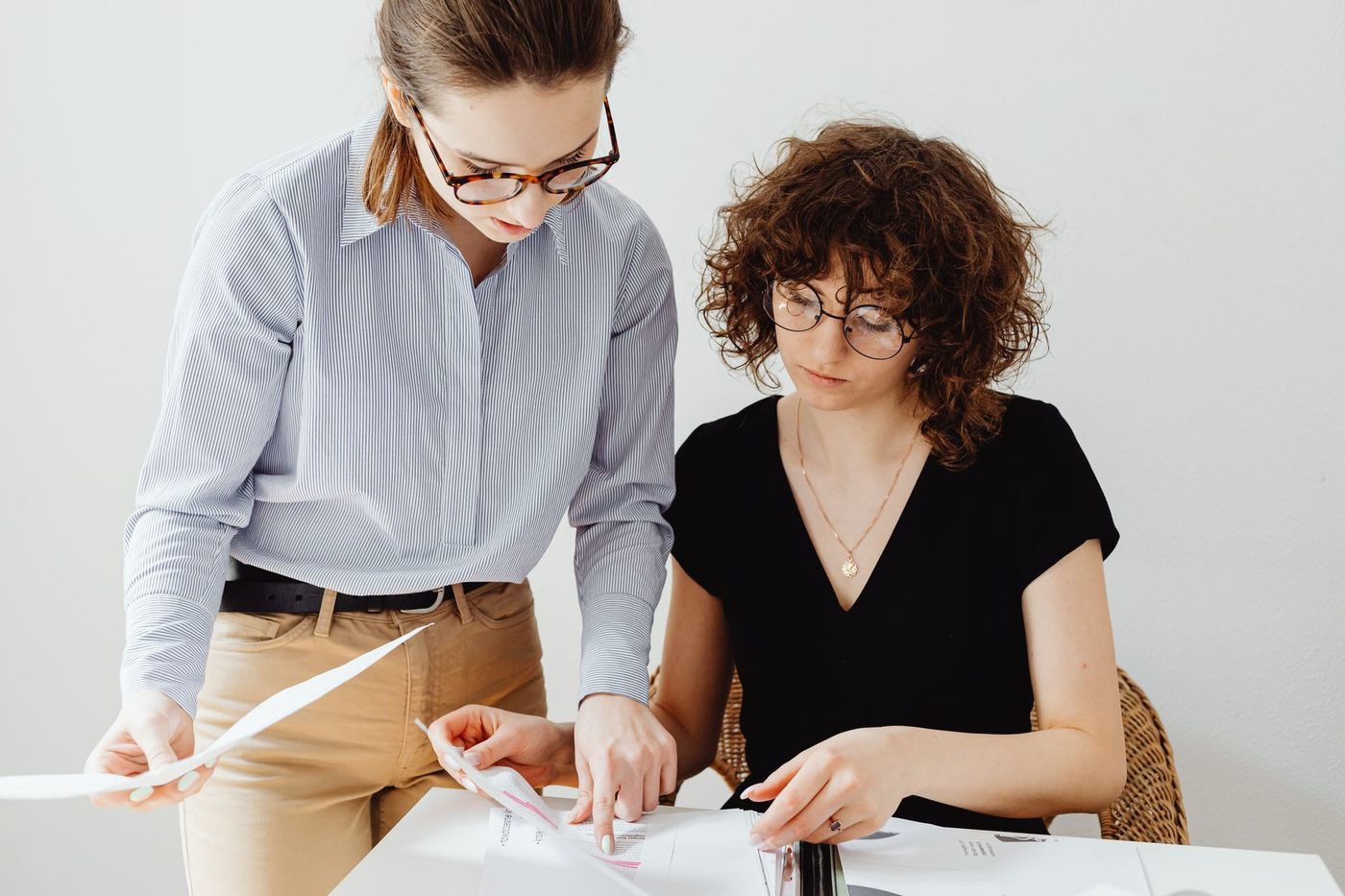 Two colleagues comparing printed contract pages at a white desk