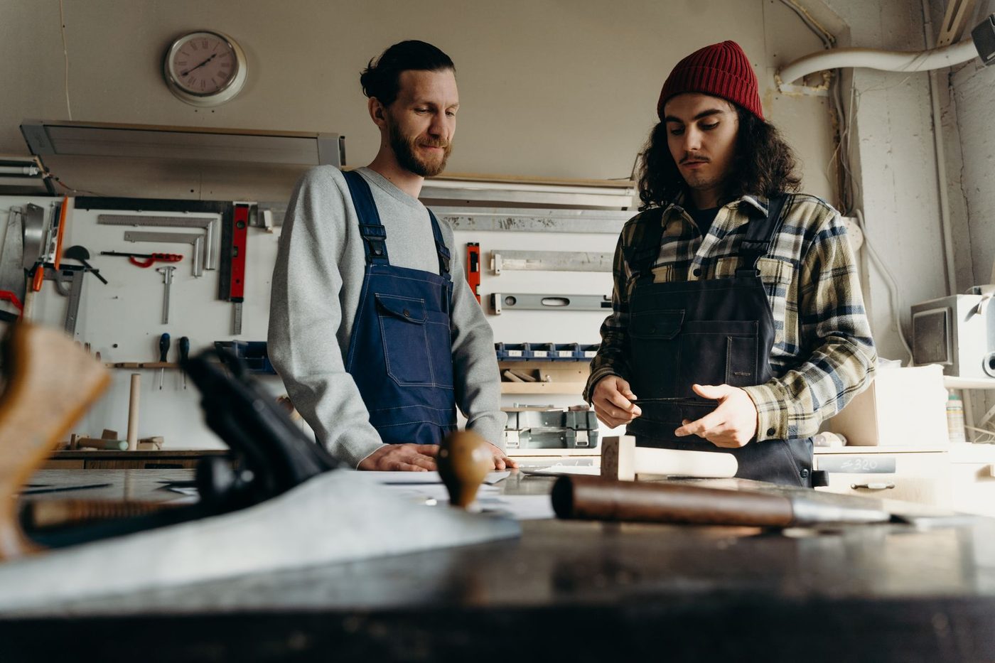 Two joiners in work overalls going over a job at a workshop bench