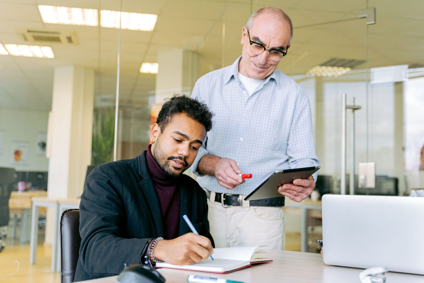 A manager with a tablet standing beside an employee who is taking notes