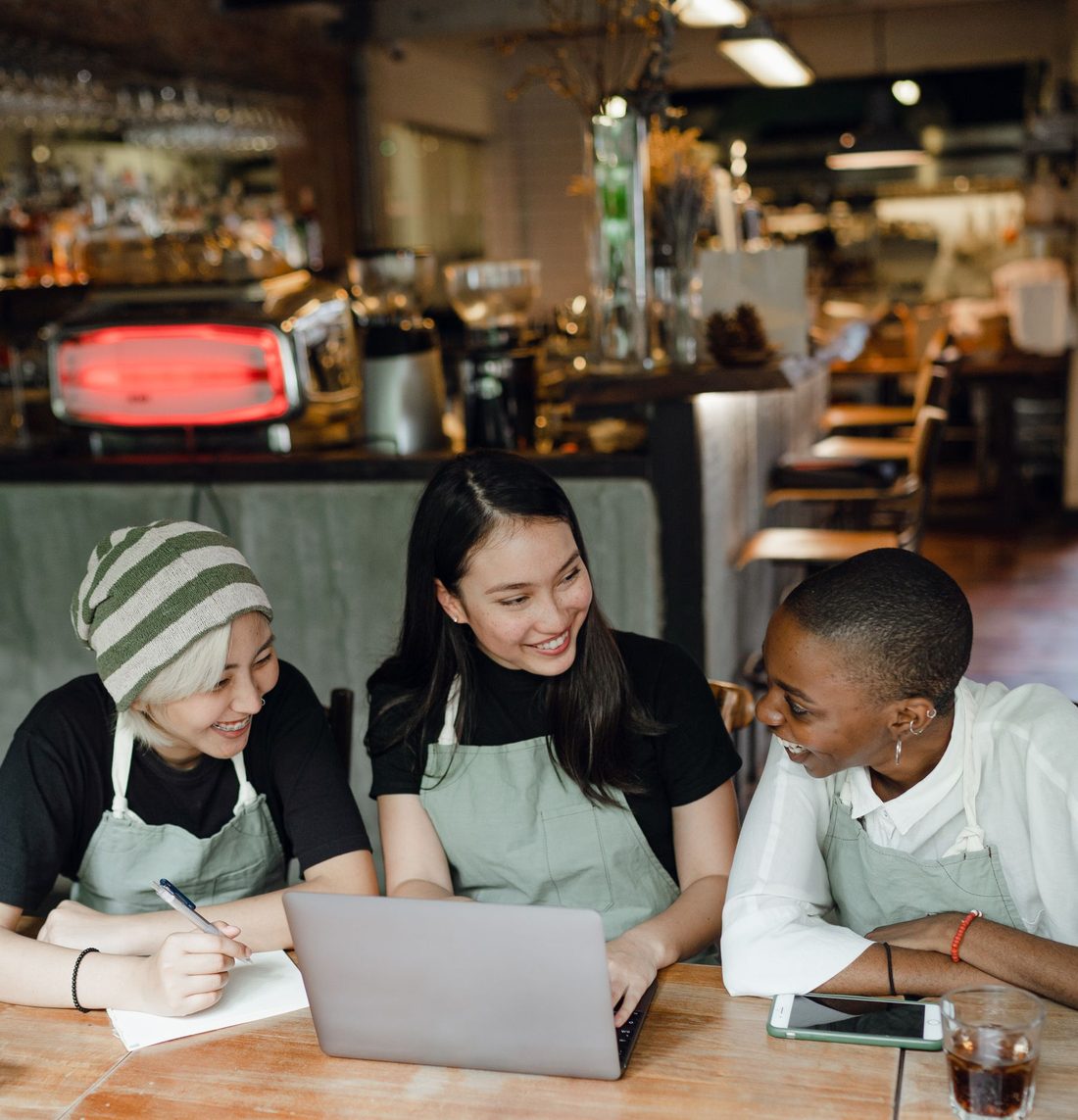 Three cafe staff in aprons sitting together at a laptop