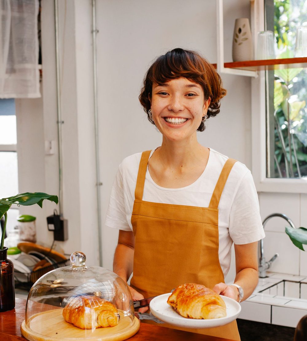 A café owner in an apron serving a croissant at her counter