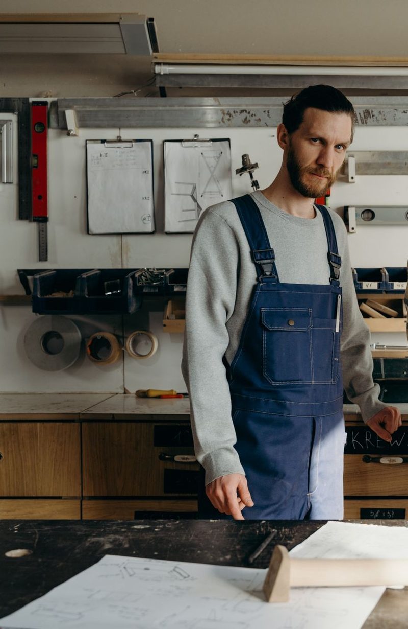 A joiner in work overalls standing at the bench in his workshop