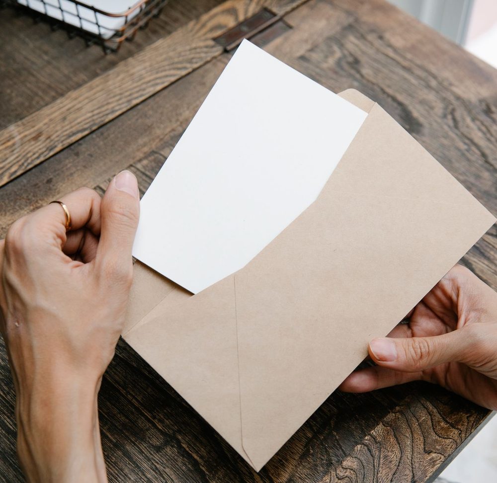 Hands opening a letter from a brown envelope at a desk