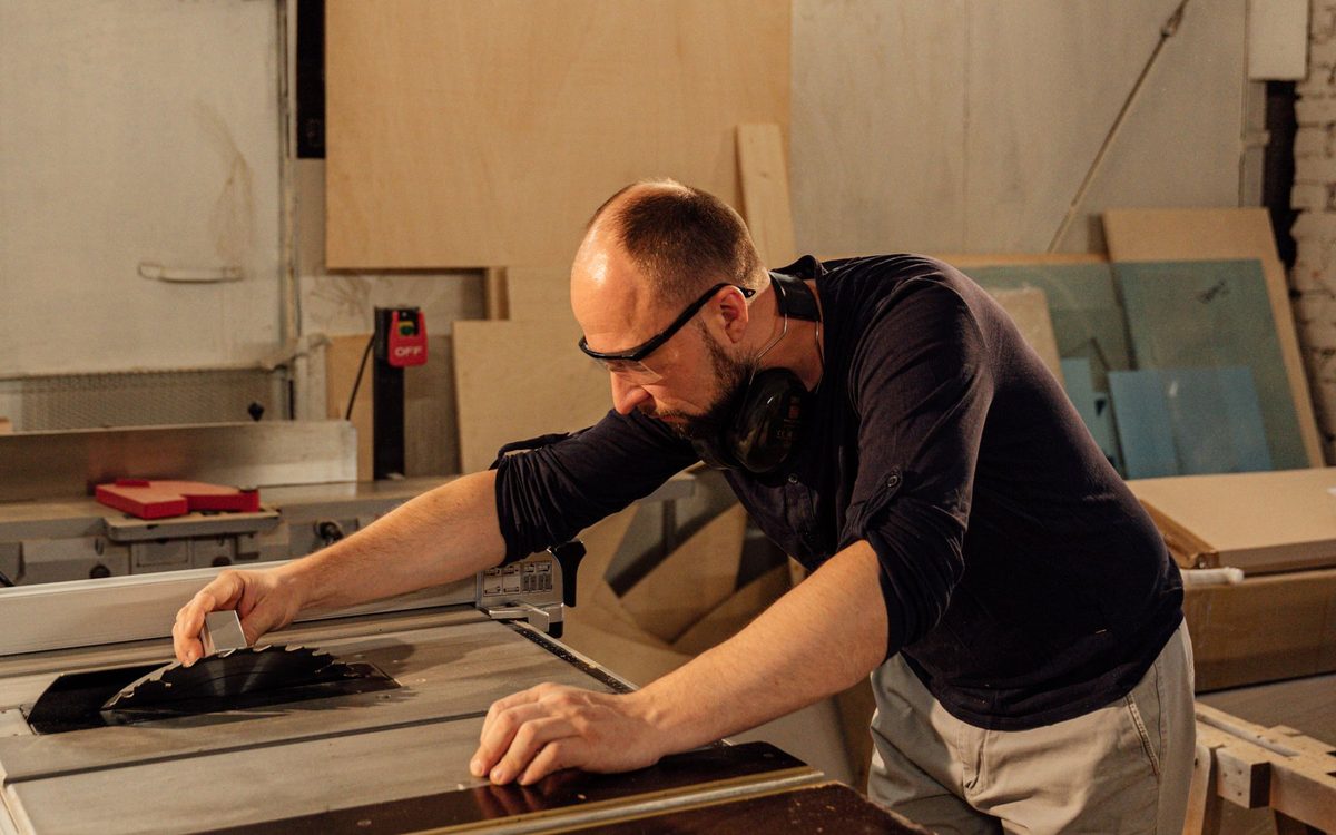 A joiner cutting a board on a table saw in a small workshop