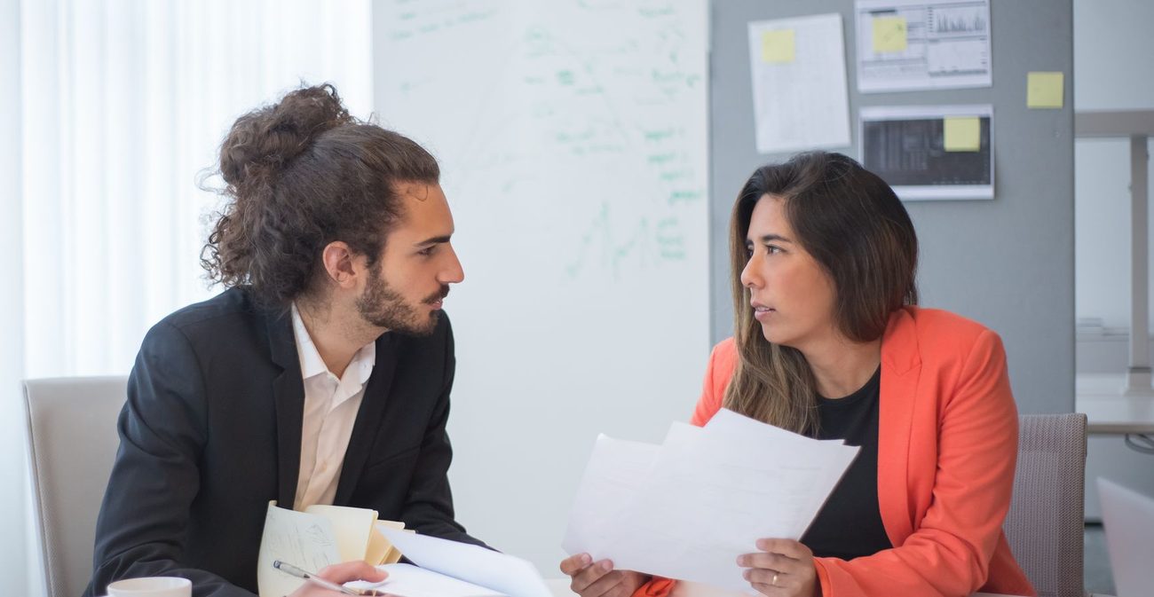 Two people from different firms comparing papers across a meeting table