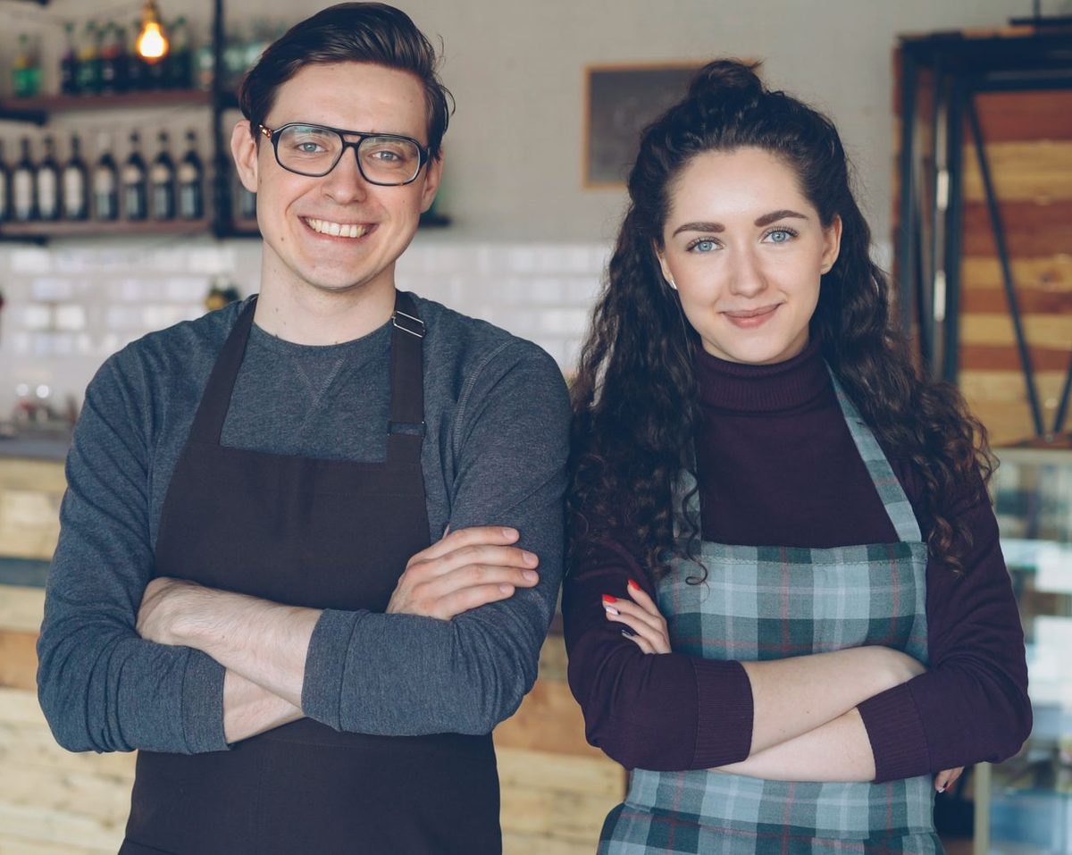 Two co-owners of a caf&eacute; standing together behind their counter