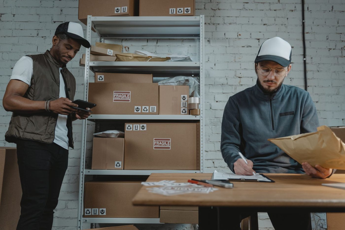Two men in a stockroom checking deliveries and paperwork beside shelves of boxes
