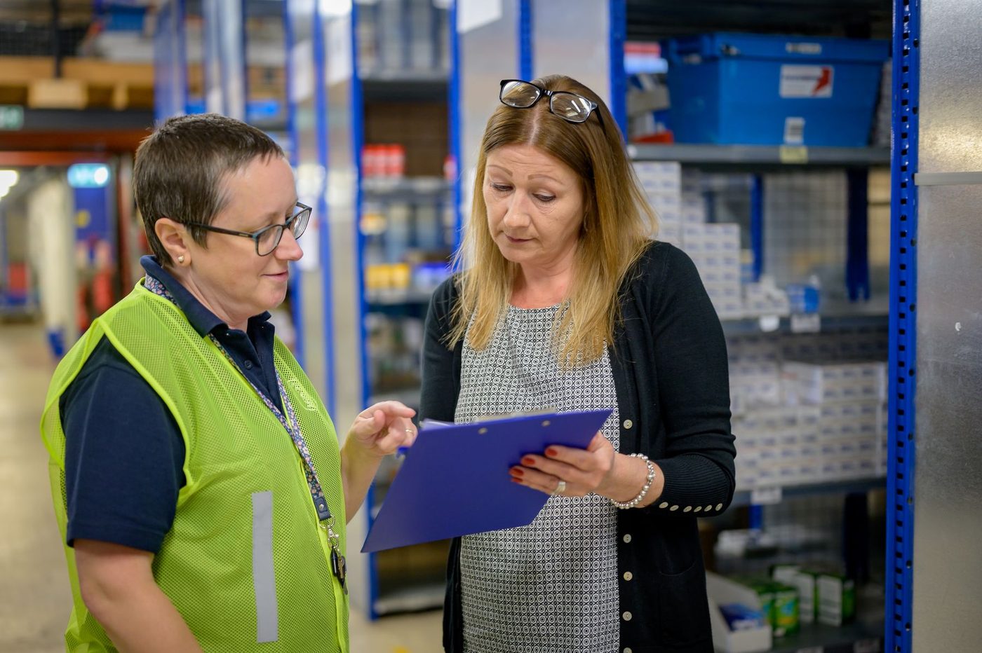 Two women in a stockroom going through paperwork on a clipboard