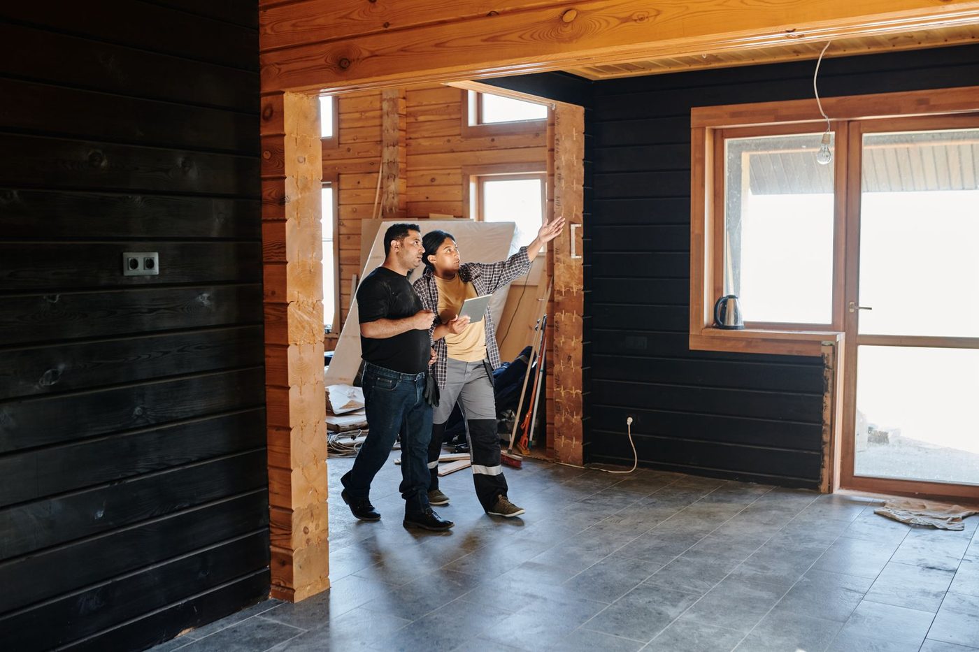 Two people walking through a timber-framed room under renovation